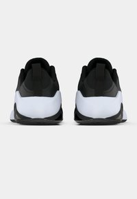 Sorte atletik sko med en hvid mellemsål og tekstureret hæl. Har en pull-tab og et mønstret hælstykke for bedre greb.