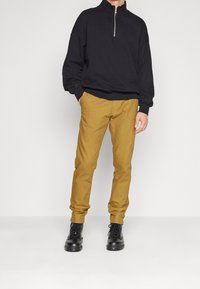 Svart zip-up hoodie med långa ärmar, kombinerad med slim fit byxor i senapsgul färg och svarta snörade stövlar. Slät tyg med avslappnad passform.