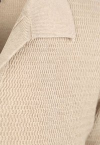 Beige gemêleerd stof met een golvende breipatroon, met een zacht, iets verhoogd gebied bij de naad voor structureel detail.