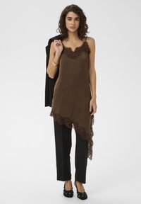 Débardeur marron orné de dentelle avec une silhouette fluide, associé à un pantalon droit noir et des chaussures noires ornées d'embellissements. Tissu texturé.