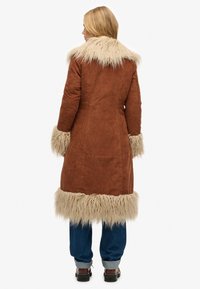 Bruine corduroy jas met een zachte beige faux-fur kraag en manchetten, halflang, met een gestructureerd ontwerp en textuurrijke accenten.