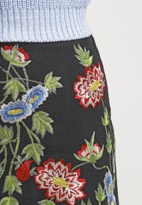 Falda de fieltro negra con bordado floral en rojo, azul y verde. Cintura acanalada de color azul claro, costuras detalladas y diseño vibrante.