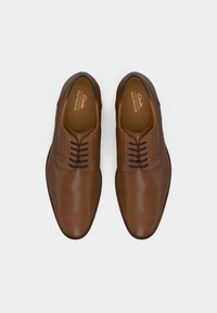 Braune Lederdressschuhe mit glatter Oberfläche, die ein schnürbares Design und dezente Nähte auf dem Obermaterial aufweisen.