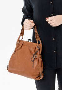 Borsa a tracolla in pelle marrone con una texture morbida, design plissettato, due manici corti e accessori metallici. Presenta una catena e un charm decorativo.