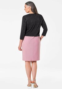 Schwarzes Shirt mit drei Viertelärmeln und funkelnder Textur, kombiniert mit einem figurbetonten rosa Bleistiftrock. Das Modell trägt silberne High Heels mit Riemchen.