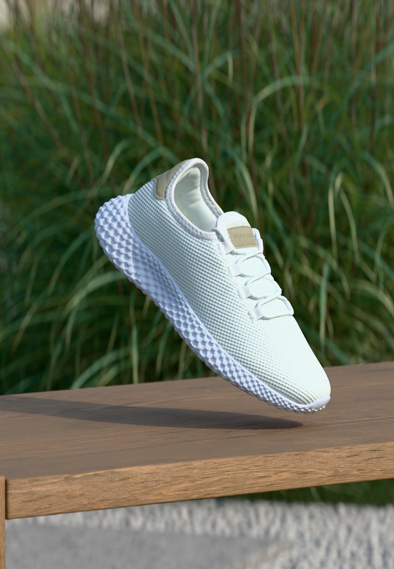 Lekki biały sneaker z siateczkową cholewką i teksturowaną gumową podeszwą; posiada tanowy akcent na pięcie i sznurowadłach.