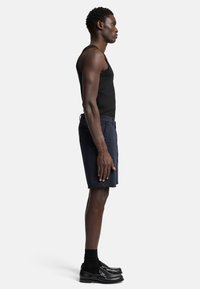Des Hauts en noir côtelé, un short bleu marine, des chaussettes noires et des chaussures noires brillantes, présentés en position de profil latéral. Design minimaliste et texture.