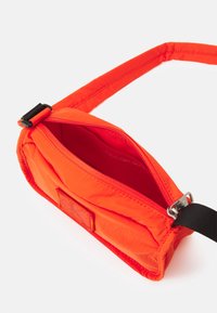 Borsa a tracolla in nylon arancione con scomparto con cerniera, tracolla regolabile e una discreta patch con logo. Superficie texturizzata con un design elegante.