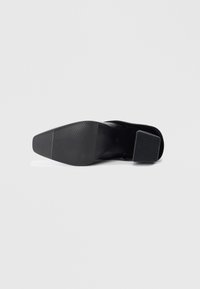 Black high-heeled shoe with a square heel, textured rubber sole, and smooth upper. Features a pointed toe and sleek, simple design.