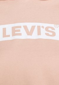 Sudadera rosa con una banda blanca en el pecho que lleva el texto "LEVI'S®" en letras negritas. La tela tiene un acabado suave y ligeramente texturizado.