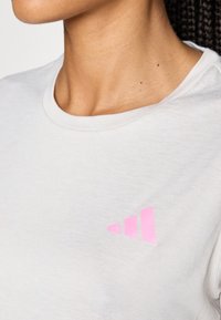 Világosszürke, rövid ujjú póló, puha anyagból, a bal oldalon kiemelkedő rózsaszín Adidas logóval. Kerek nyakkivágás.