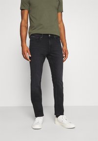 Mörk denimjeans med en slim-fit design. Har en framtill knäppning med knapp, fem fickor och subtila sömnadsdetaljer. Bärs med en grön t-shirt.