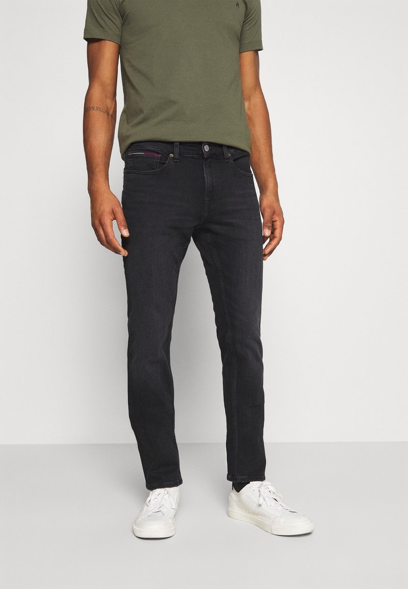 Mörk denimjeans med en slim-fit design. Har en framtill knäppning med knapp, fem fickor och subtila sömnadsdetaljer. Bärs med en grön t-shirt.