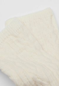 Cremfarbene gestrickte Socken mit einem strukturierten Zopfmuster. Der Stoff wirkt weich und dehnbar und hat gerippte Bündchen am oberen Ende.