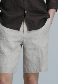 Shorts en lin beige clair avec une coupe décontractée, des poches latérales et des ourlets retournés. Associés à une chemise boutonnée marron foncé.