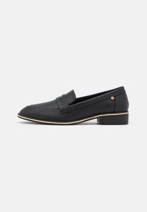 Sort læder loafer med lav hæl, rundet tå, dekorativ strop over vristen og tynd beige kant over sålen.