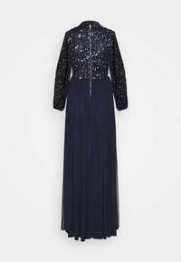 Largo vestido azul marino con un corpiño ajustado de lentejuelas, cuello alto y mangas largas. La falda plisada y fluida se extiende por debajo de la cintura, con un cierre de cremallera.