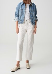 Chaqueta de denim azul claro con cierre de botones, combinada con jeans blancos de tiro medio. Mocasines beige completan el conjunto. Texturas suaves y estilo casual.