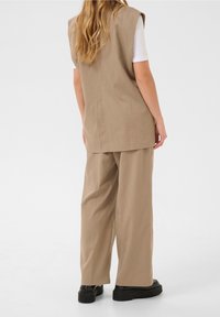 Beige ärmellose Weste und passende weit geschnittene Hose aus glattem Stoff. Das Outfit zeichnet sich durch ein einfaches Design und eine lockere Passform aus.