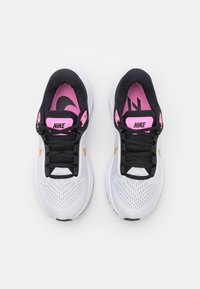 Scarpe da ginnastica bianche con una tomaia in rete traspirante, accenti neri, marchio rosa e una swoosh dorata. Presenta una suola ammortizzata e lacci neri.