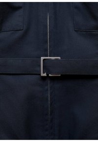 Tissu bleu marine à texture lisse, avec une fermeture éclair centrale et une ceinture avec une boucle en métal argenté pour une fixation sécurisée.