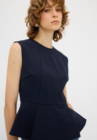 Top peplum blu navy con scollatura rotonda e maniche corte, caratterizzato da un corpetto aderente e un tessuto morbido e strutturato.