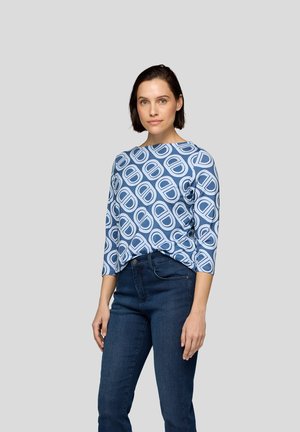 Blouse bleue à motifs avec un col bateau et des manches trois-quarts, présentant un design géométrique en bleu clair sur un fond bleu foncé.