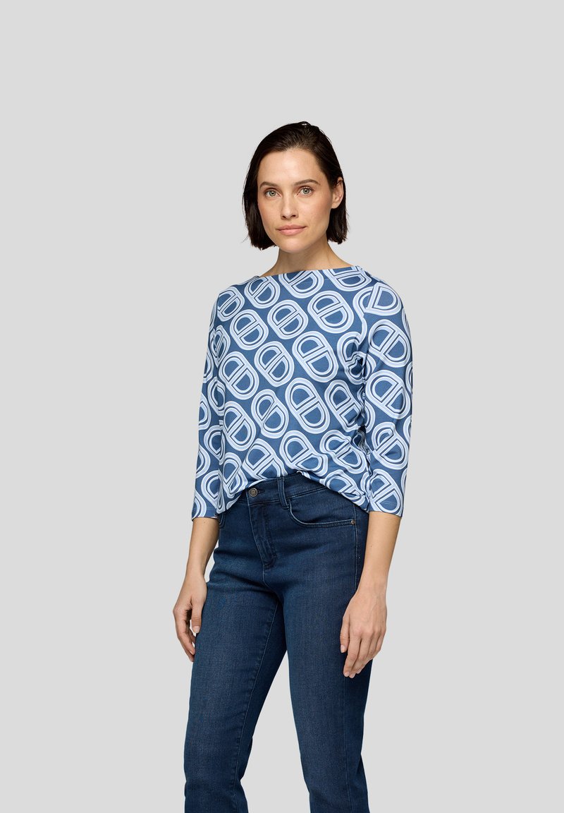 Blaue gemusterte Bluse mit einem U-Boot-Ausschnitt und dreiviertel Ärmeln, die ein geometrisches Design in hellblau auf einem dunkelblauen Hintergrund zeigt.