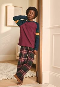 Long-sleeve maroon top with blue, green, and yellow accents paired with plaid pajama pants in deep green and burgundy tones.