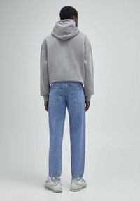 Felpa grigia con cappuccio, jeans azzurri chiari, tessuto testurizzato, vestibilità comoda e cuciture visibili; indossata con sneakers grigie e bianche.