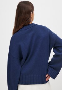 Navy blue knitted sweater with a ribbed hem and cuffs. Features a relaxed fit and wide, dropped shoulders. Textured fabric with a smooth finish.