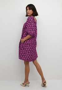 Kurzärmliges, knielanges Kleid im lebhaften rosa-lila Blumenmuster. Mit runder Rückenpartie und seitlichen Taschen. Aus leichtem Stoff gefertigt.
