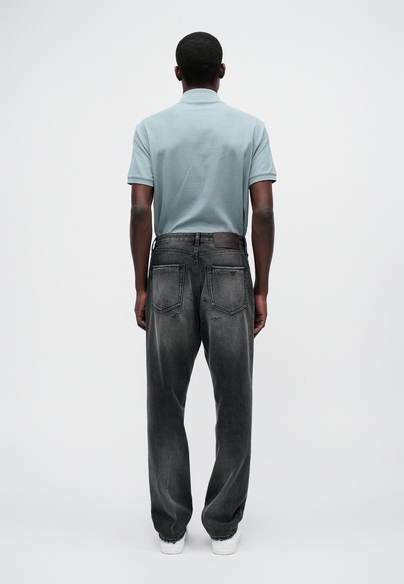 Polo bleu clair associé à un jean décontracté gris foncé. Le jean présente une texture délavée et une patch en cuir à l'arrière de la taille.