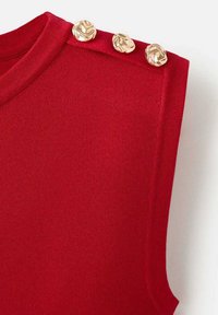 Haut rouge sans manches avec une coupe ajustée. Il présente un col rond et trois boutons décoratifs dorés sur l'épaule. Texture lisse.