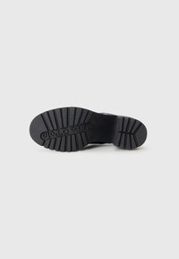 Soletta di scarpa in gomma nera con un motivo di battistrada testurizzato e il nome del marchio inciso "Marco O'Polo." Presenta un design piatto per la stabilità.