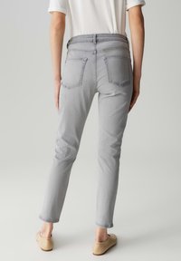 Jeans skinny en denim gris avec cinq poches, une taille mi-haute et une légère élasticité. Portés avec des ballerines beige clair, longueur cheville avec des ourlets roulés.