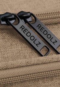 Borsa di tessuto color cammello con due cursori neri della cerniera etichettati "REDOLZ." I dettagli includono una trama testurizzata e una linea della cerniera liscia.