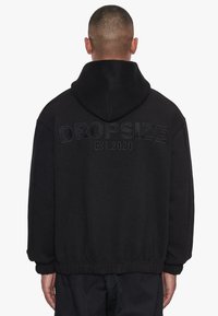 Schwarzer Kapuzenpullover mit gerippten Bündchen und Saum, bestickt mit "DROPSIZE EST. 2020" auf dem Rücken, aus einem weichen Stoff gefertigt.