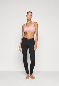 Ljust rosa sportbh med en slät yta och breda band, parat med tätt sittande svarta leggings med en mjuk midja och minimal logotyp.