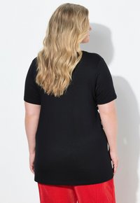 Top corto negro de manga corta hecho de una tela suave, con un corte relajado, combinado con pantalones texturizados rojos brillantes.