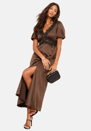 Braunes Satinkleid mit Spitzenbesatz, V-Ausschnitt, kurzen Puffärmeln, seitlichem Schlitz, kombiniert mit einem schwarzen Clutch und schwarzen, mit Riemchen versehenen High Heels.