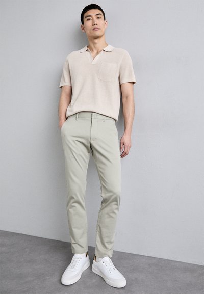 Beige stickad polo skjorta med ficka, tillsammans med ljusgröna smalrandiga byxor och vita sneakers. Enkel design, släta texturer och neutrala färger.