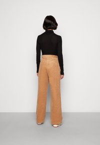 Ljust bruna sammetsbyxor med vida ben, med hög midja och vertikal ribbad textur, i kombination med en figurnära svart långärmad topp.