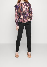 Blusa de manga larga con estampado floral en púrpura oscuro y acentos brillantes; Jeans ajustados negros; Tacones marrones con tiras; Textura suave.
