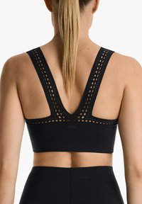 Czarny stanik sportowy z designem w kształcie litery V na plecach oraz wycięciami, wykonany z gładkiego materiału z minimalnym brandingiem na oraz.