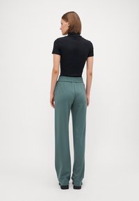 Must have lühikeste varrukatega must turtleneck, mille juurde on sobitatud kõrge vöökoht ja laiemad salve roheline püksid, millel on elastne vöökoht ja tekstuuriga kangas.