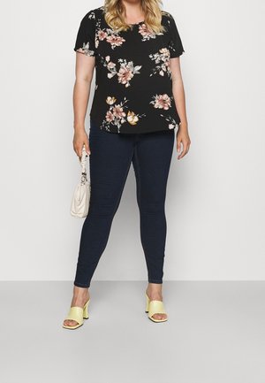 Top floreale nero con maniche corte, jeans scuri, sandali a blocco gialli e borsa color crema. Presenta motivi floreali rosa e crema.