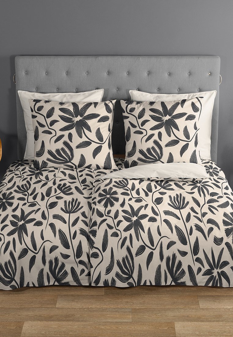 Set di copripiumini con motivi floreali neri su uno sfondo crema, completo di cuscini decorativi e una testata imbottita grigia chiara.