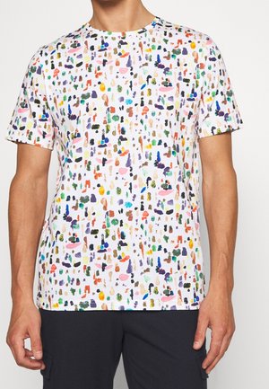 Mann trägt ein weißes T-Shirt mit kurzen Ärmeln und einem bunten abstrakten Farbspritzmuster sowie schwarze Hose.