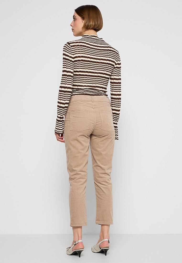 Braun gestreiftes Langarmoberteil, beige Cordhosen, taillierte Passform, sichtbare Gesäßtaschen und hellfarbene Absätze.
